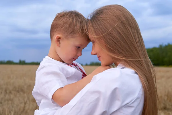 Ritratto di figlio allegro con macchina fotografica seduta sulle ginocchia delle madri in mezzo al campo di grano. — Foto Stock