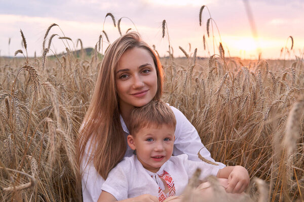 Portrait of cheerful son with camera sitting on mothers laps amidst wheat field.