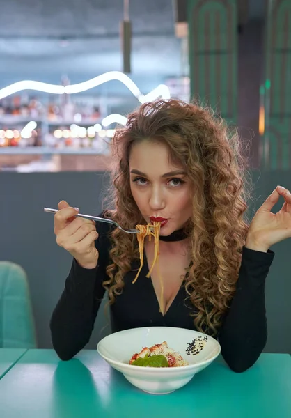 Cute girl with curly hair eating pasta in a restaurant. — Stock Photo, Image