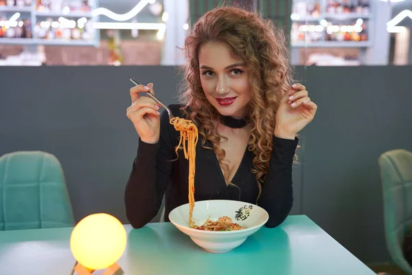 Söt flicka med lockigt hår äter pasta i en restaurang. — Stockfoto