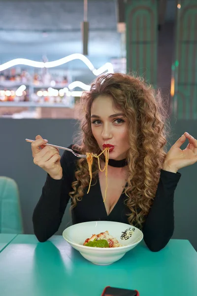 Cute girl with curly hair eating pasta in a restaurant. — Stock Photo, Image