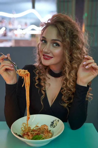 Söt flicka med lockigt hår äter pasta i en restaurang. — Stockfoto