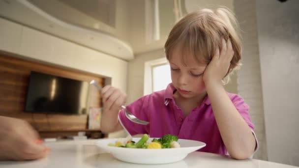 Pojken försöker äta en grönsak men doftar som den och avvisar maten. Hälsosam mat koncept. Barn och grönsaker. — Stockvideo