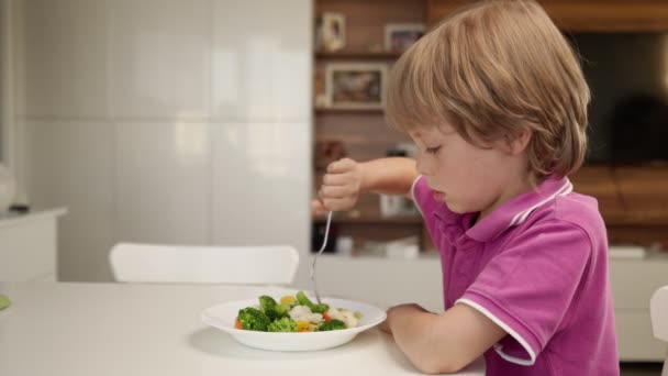 Junge versucht, ein Gemüse zu essen, aber Dosis mag es und lehnt das Essen ab. Gesundes Essen. Kinder und Gemüse. — Stockvideo