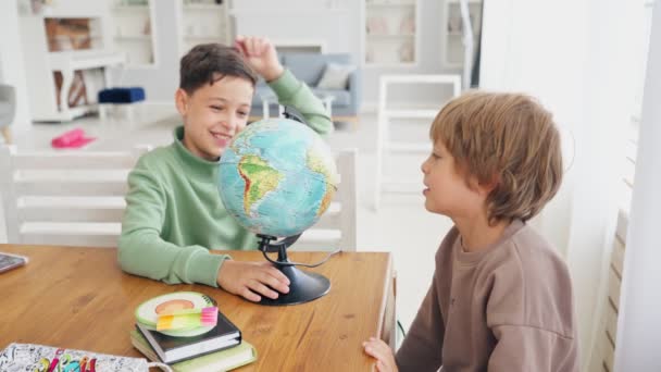 Two caucasian teen boy in lightroom playing with world globe. Children learn geography. Travel concept — Stock Video