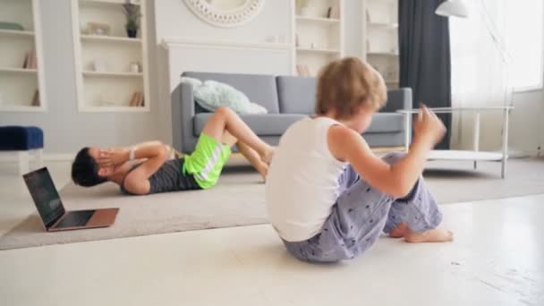 To kaukasiske gutter som trener, pusher opp og tar på seg trøkk sammen på gulvet hjemme. Nettopplæring for barn. – stockvideo