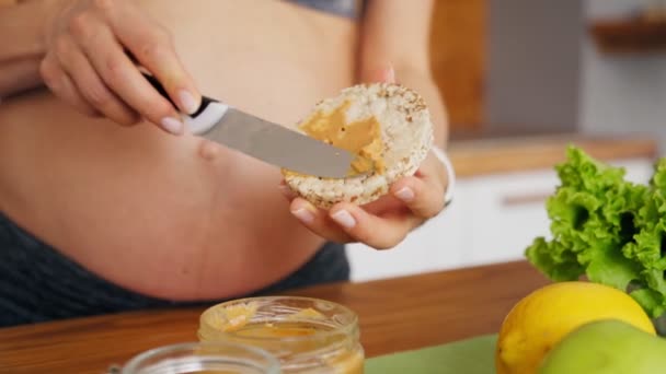 Schwangere bereitet Sandwich mit Erdnussbutter und Reiswaffel zu. Ernährungslaunen schwangerer Frauen — Stockvideo