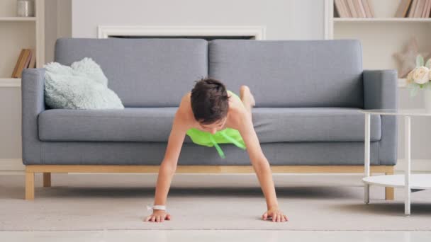 El chico con el torso desnudo comienza bruscamente a hacer fuertes flexiones en sus manos en casa sobre el fondo del sofá — Vídeos de Stock