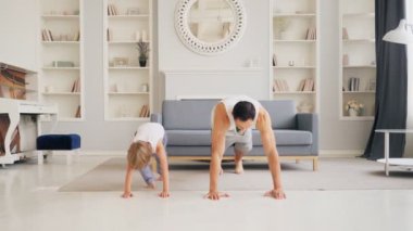 Aktif aile sağlıklı bir yaşam için oturma odasında sabah egzersizi yapıyor. Babam küçük şirin çocuğa şınav çekmeyi öğretiyor. Formda baba ve oğul evde spor yapıyor.