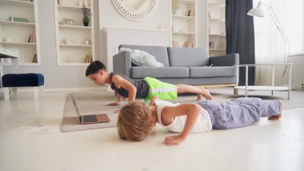 Два кавказских мальчика делают физические упражнения отжимания и пресс хрустит вместе на полу дома. Онлайн-обучение для детей. — стоковое видео