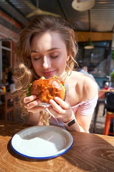 Красивая белая женщина ест вкусный бургер в солнечный день — стоковое фото