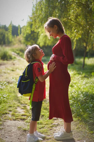 Menino pequeno tocando barriga de sua mãe grávida ao ar livre. — Fotografia de Stock
