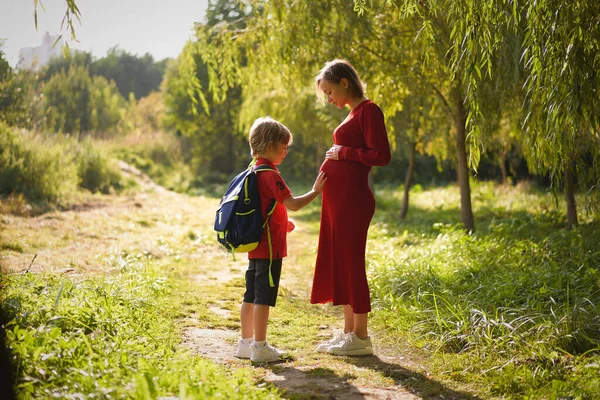 Liten pojke vidrör magen på sin gravida mor utomhus. — Stockfoto