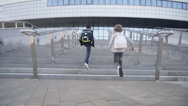 Школьники с рюкзаками бегут наверх в школу на уроки. Вид сзади — стоковое видео