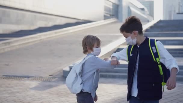 Happy schoolboys in medical mask meet in school yard and greet their elbows after the coronavirus epidemic. Young guys and new life in covid-19 or coronavirus. Social distancing together concept — Stock Video