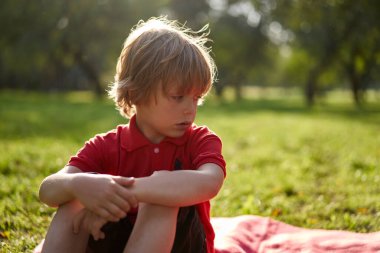 Parkta çimenlerde oturan depresyonlu yalnız çocuk.