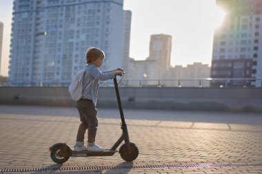 Güneşli bir günde şehirde elektrikli scooterıyla gezen okul çocuğu..