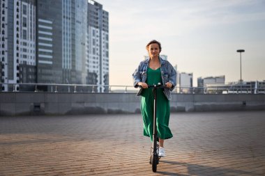 Şehirde elektrikli scooter kullanan kaygısız genç bir kadın..