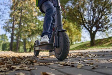 Çocuk parktan elektrikli scooterla geçiyor..