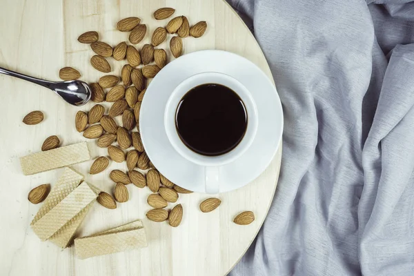 Coffee, almonds, sweets, wafers placed on a wooden floor