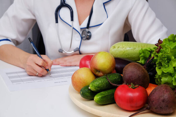 Питательница пишет план диеты на столе, полном фруктов и овощей

