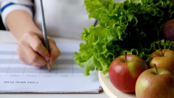 Voedingsdeskundige vrouw schrijven dieetplan op tafel vol met groenten en fruit — Stockvideo