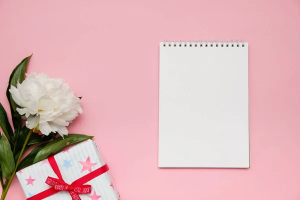 Composición con flores, regalo y cuaderno sobre fondo rosa. Prepárate para tu diseño. Puesta plana . — Foto de Stock