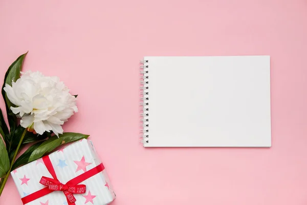 Composición con flores, regalo y cuaderno sobre fondo rosa. Prepárate para tu diseño. Puesta plana . — Foto de Stock