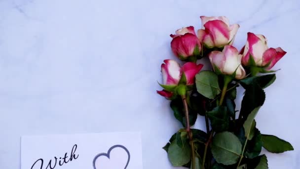 Med kärlek gratulationskort, gåva och blommor på vit tavla, ovanifrån — Stockvideo