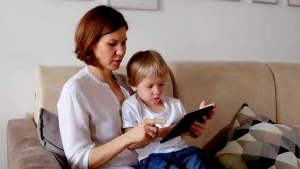 女人坐在沙发上和她的儿子玩平板电脑 — 图库视频影像