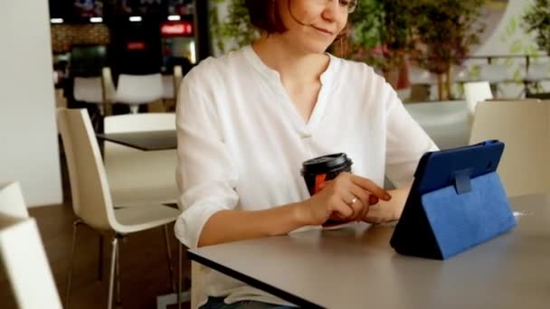 Woman working with tablet pc and drinking coffee at the food court — Stock Video