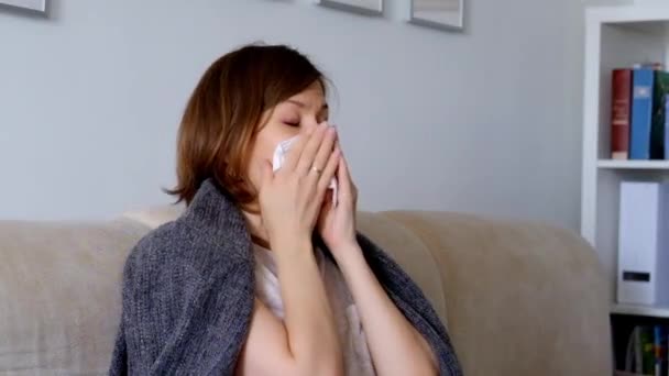 Женщина, сидящая на диване, чувствует себя плохо и чихает — стоковое видео