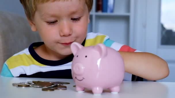 Маленький мальчик кладет монеты в копилку — стоковое видео
