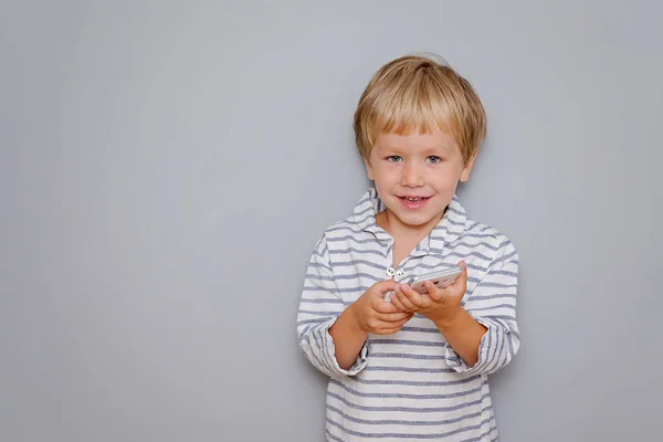 Lindo niño de tres años sosteniendo teléfono inteligente sobre fondo gris con espacio de copia — Foto de Stock