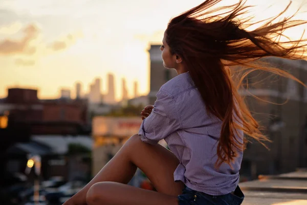 Mulher bonita com cabelo vermelho sentado em um telhado ou ponte, luz do pôr do sol — Fotografia de Stock