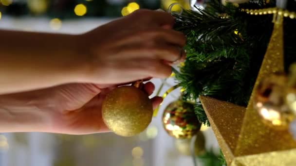 Womans hands adorn Christmas tree by golden toy. Fairy lights on background . — Stock Video