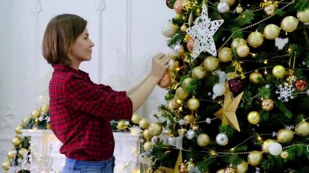 Vrouw versieren kerstboom van gouden speelgoed op de kamer — Stockvideo