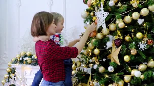 Frau mit Sohn schmückt Weihnachtsbaum mit goldenem Spielzeug im Zimmer — Stockvideo