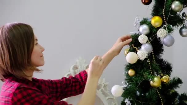 Vrouw versieren kerstboom van gouden speelgoed op de kamer — Stockvideo