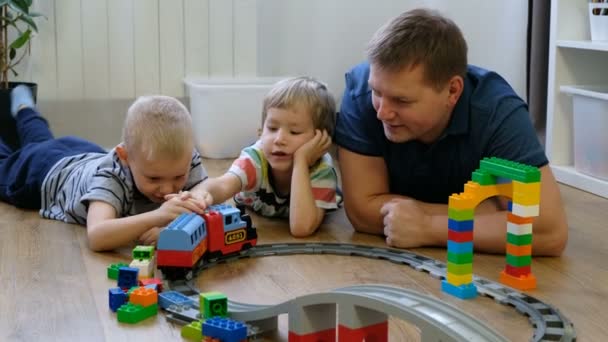 Familienkonzept. Jungen und Väter spielen mit Zügen auf Holzboden. Vater mit Söhnen — Stockvideo