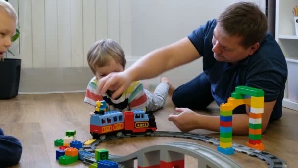 Familjen koncept. Pojkar och pappa leker med tåg på trägolv. Far med söner — Stockvideo