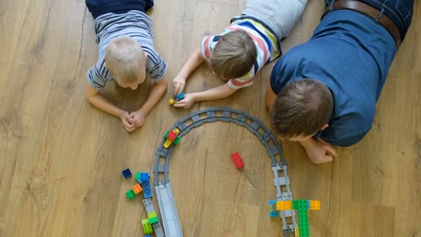 Семейная концепция. Мальчики и папа играют с поездами на деревянном полу. Отец с сыновьями. Прямо над видом — стоковое видео