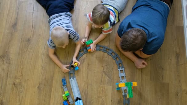 Concepto familiar. Chicos y papá jugando con trenes en el suelo de madera. Padre con hijos. Directamente encima de la vista — Vídeo de stock