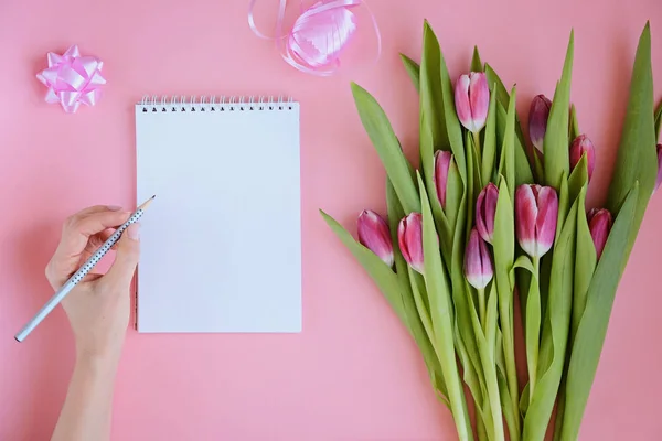 Estilo plano femenino con flores de tulipán rosa, cuaderno y las manos de las mujeres — Foto de Stock