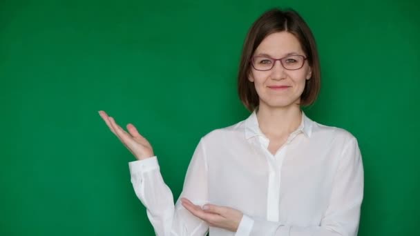 Mulher sorridente bonita em óculos e blusa branca apontando para a direita na tela verde, chave Chroma — Vídeo de Stock