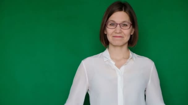 Schöne lächelnde Frau mit Brille und weißer Bluse, die auf grünem Bildschirm nach rechts zeigt, Chroma-Taste — Stockvideo