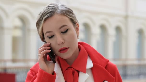 Joven mujer de negocios confiada en abrigo rojo hablando por teléfono — Vídeo de stock