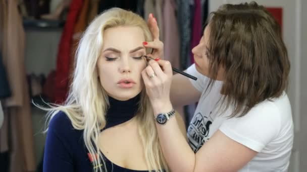 Artista de maquillaje profesional trabajando con una hermosa mujer joven — Vídeo de stock