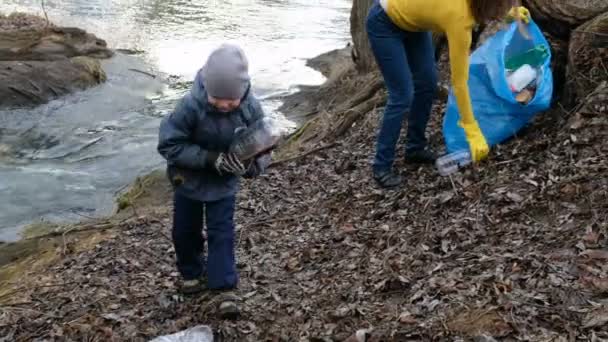 Жінка-доброволець зі своєю дитиною прибирає сміття біля річки. Екологія та концепція навколишнього середовища — стокове відео