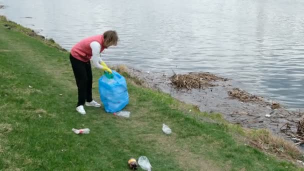 Жінка-доброволець прибирає сміття біля річки. Збирати сміття на відкритому повітрі. Екологія та концепція навколишнього середовища — стокове відео